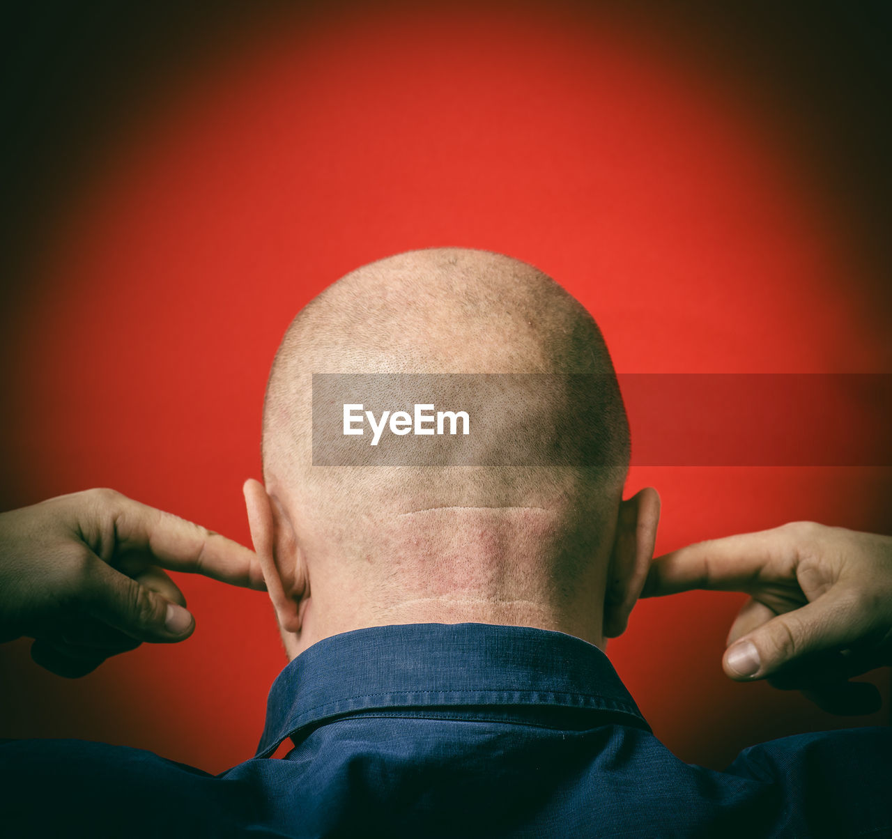 Rear view of mature man with fingers in ears against red background