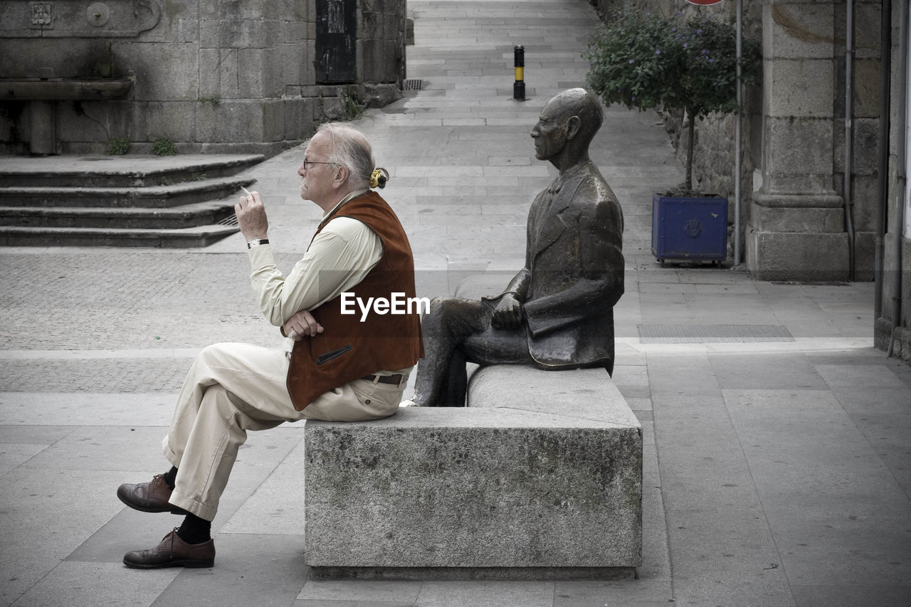 REAR VIEW OF MAN SITTING ON BENCH AT STAIRCASE