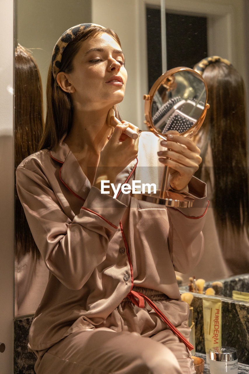 Portrait of young woman using mirror make-up