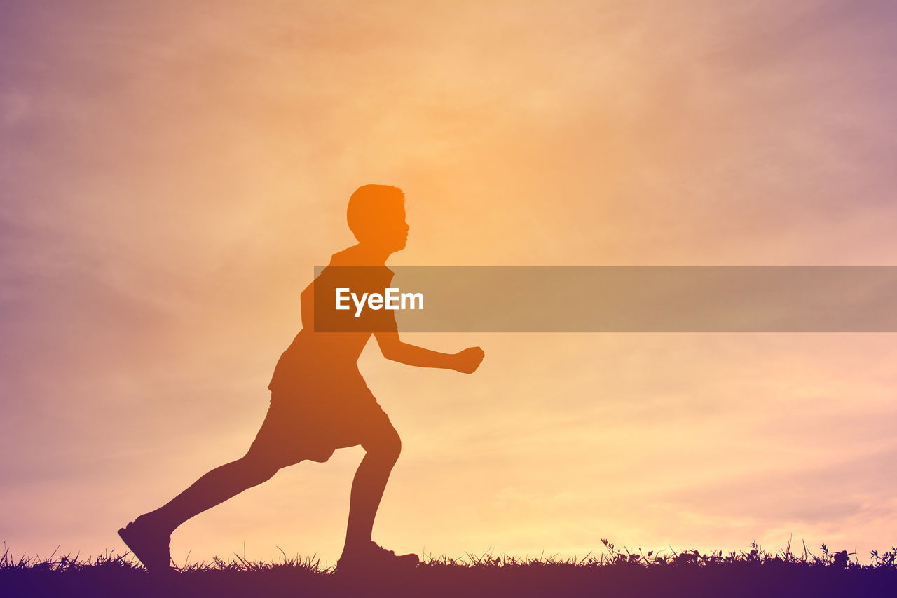 Silhouette boy running on field against sky during sunset