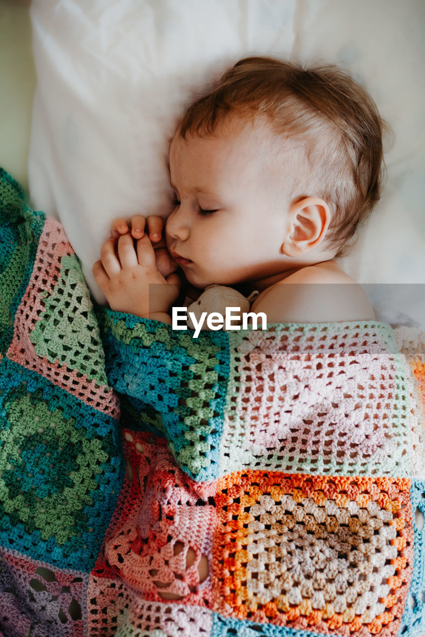 Cute baby sleeps peacefully in crib with handle under his cheek. one year old boy laying covered