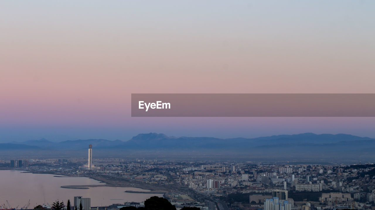 HIGH ANGLE VIEW OF BUILDINGS IN CITY AGAINST SKY DURING SUNSET