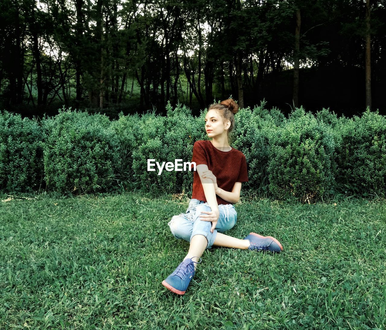 Young woman sitting on grassy field against trees