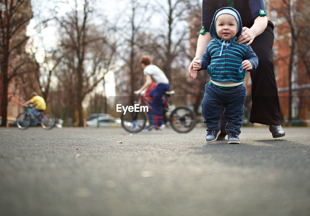 Low section of mother assisting baby boy walking on street