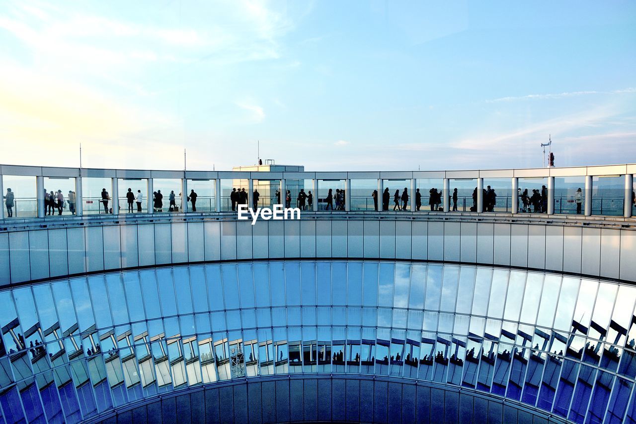 People by railing against blue sky