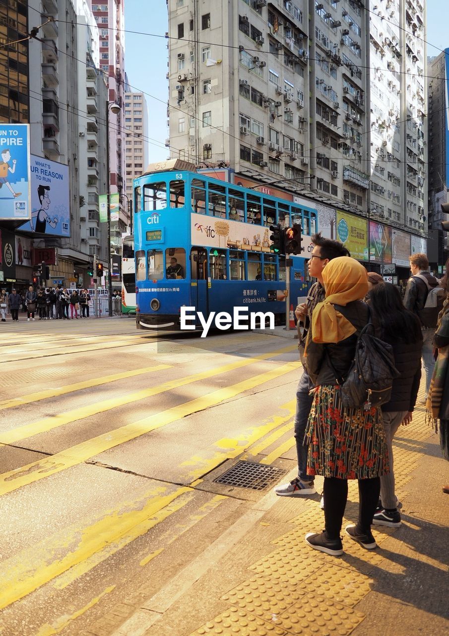 REAR VIEW OF PEOPLE STANDING ON STREET