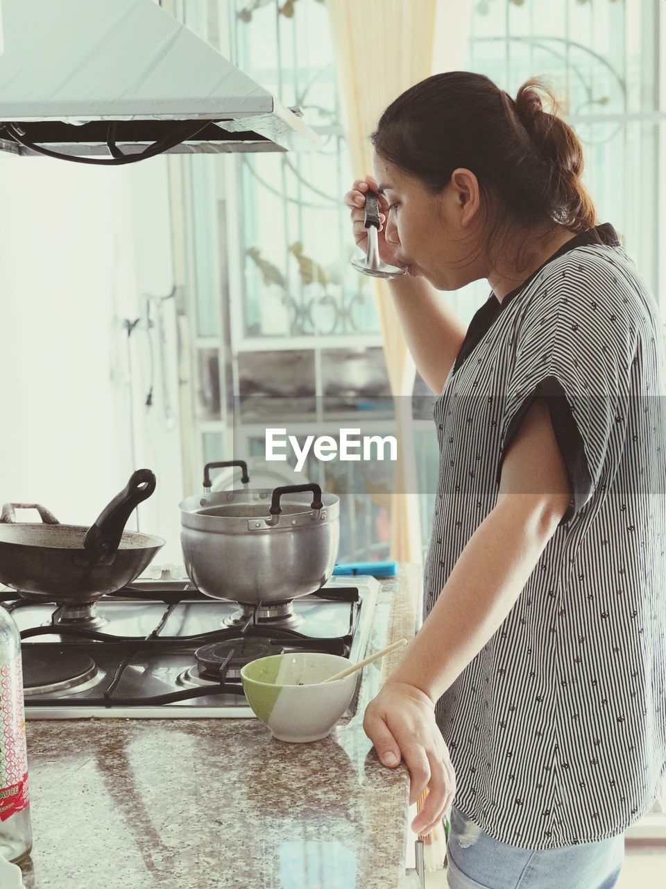 Side view of woman tasting food while standing at kitchen counter