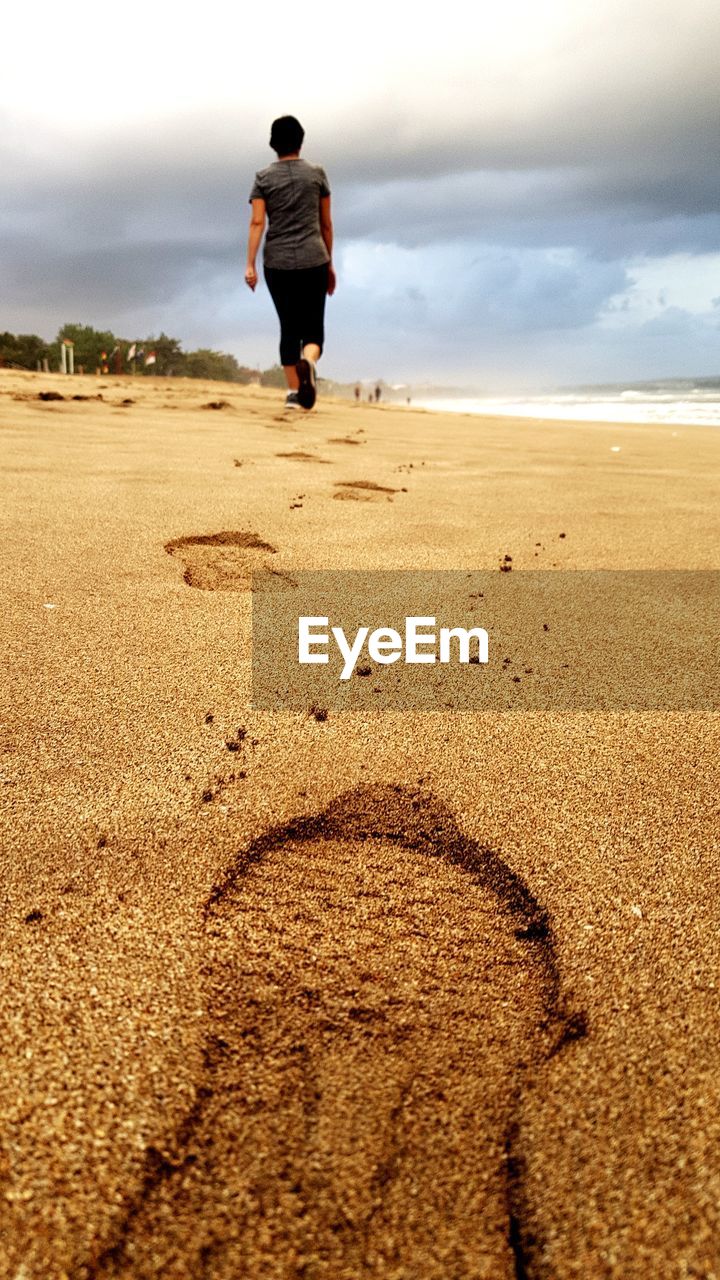 FULL LENGTH REAR VIEW OF WOMAN STANDING ON BEACH AGAINST SKY