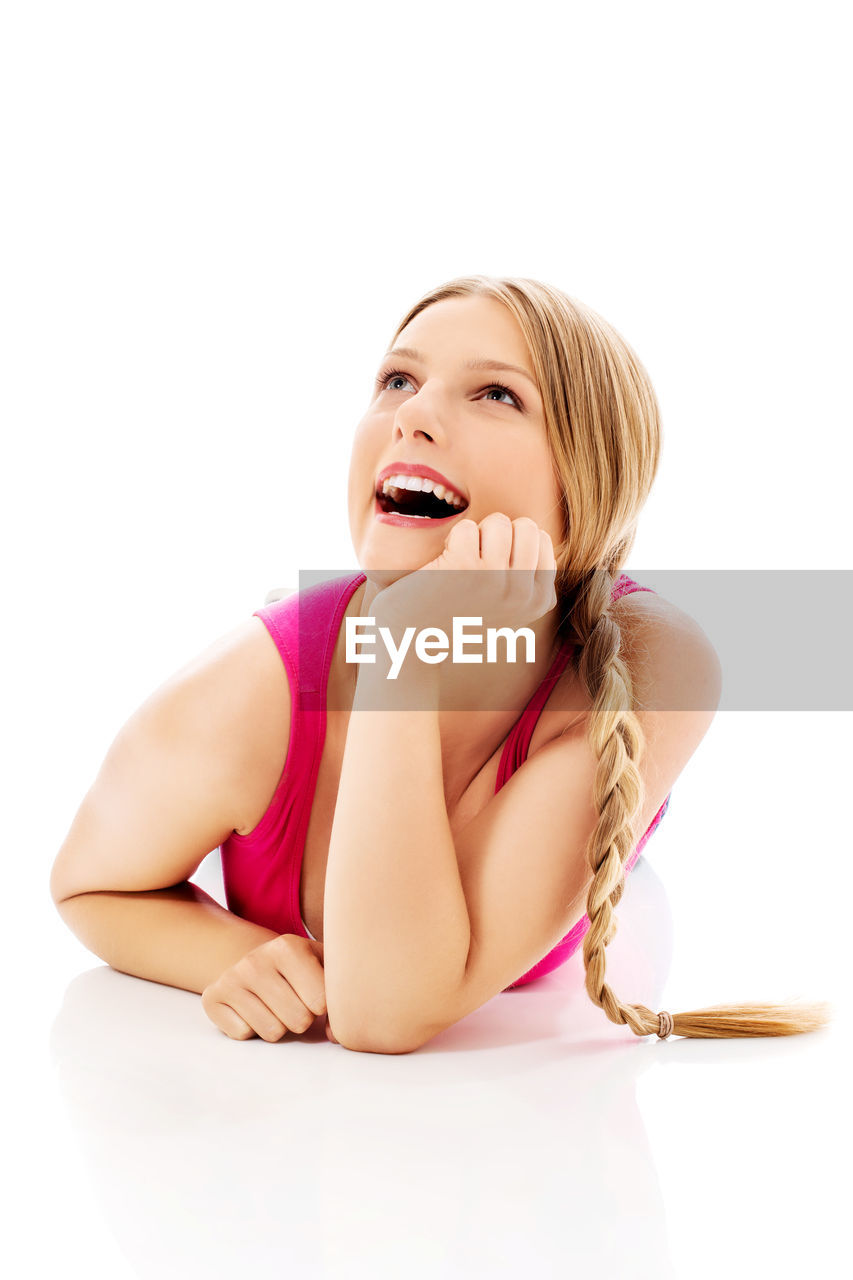 Young woman with hand on chin laughing while lying on white background