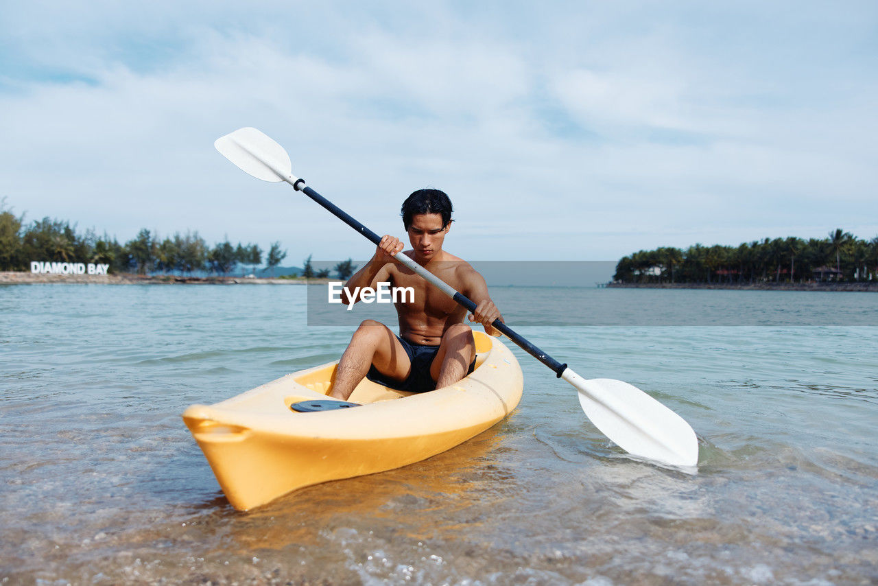 man kayaking in sea against sky