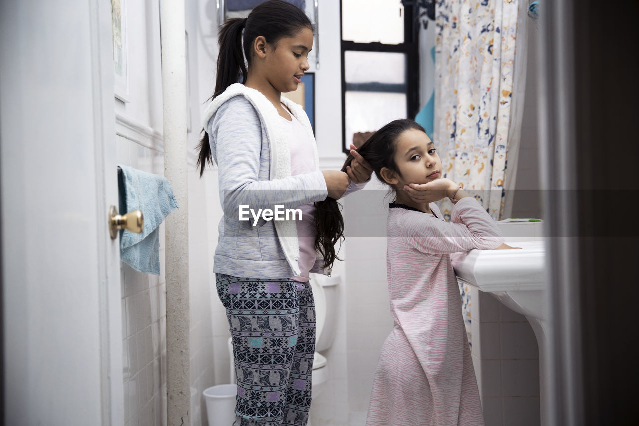 Girl tying hair of sister while standing in bathroom