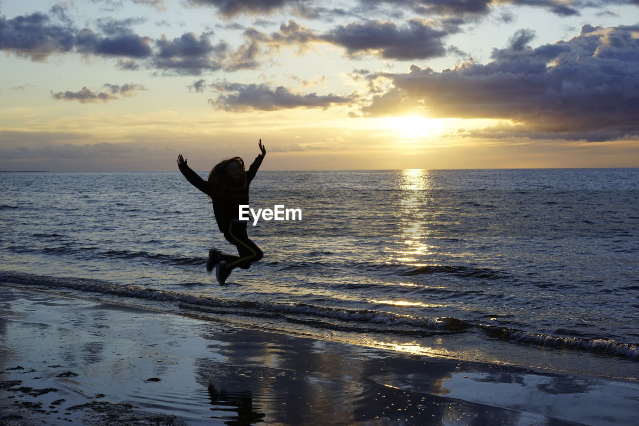 WOMAN JUMPING AT BEACH DURING SUNSET