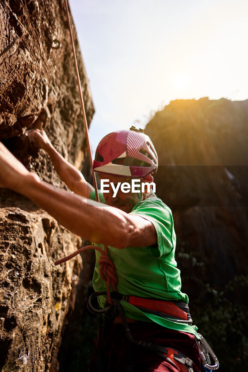 From below side view unrecognizable active fit senior man climbing on rocky cliff