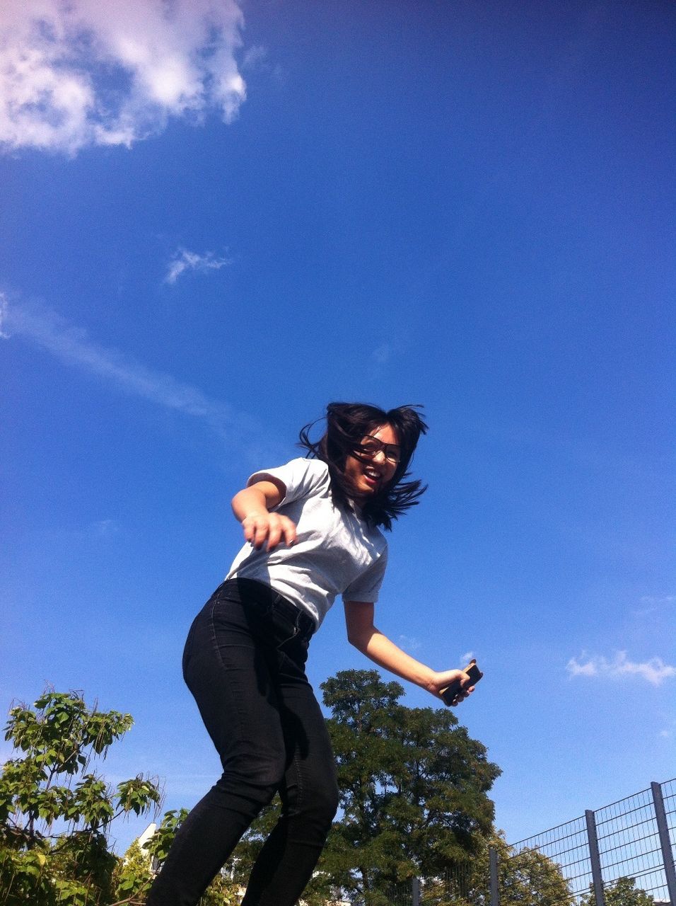 Low angle view of cheerful young woman jumping against blue sky