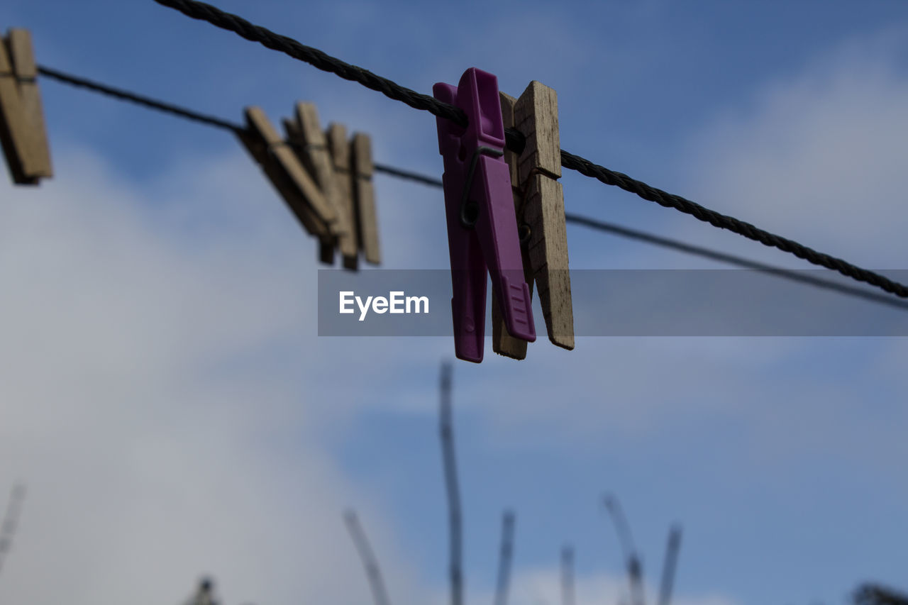 Clothespins hanging on clothesline against sky