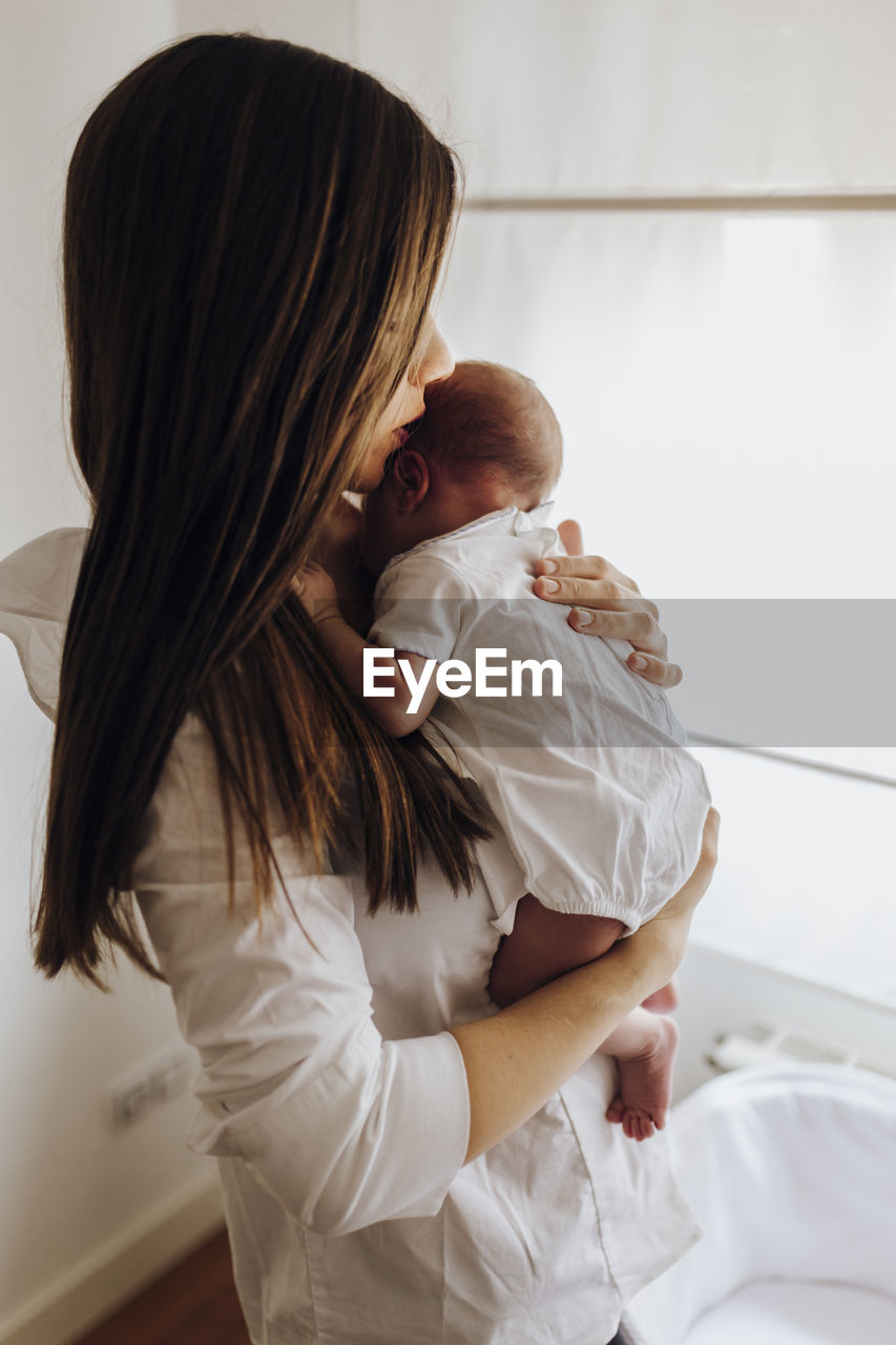 Close up young mum kissing newborn baby on forehead