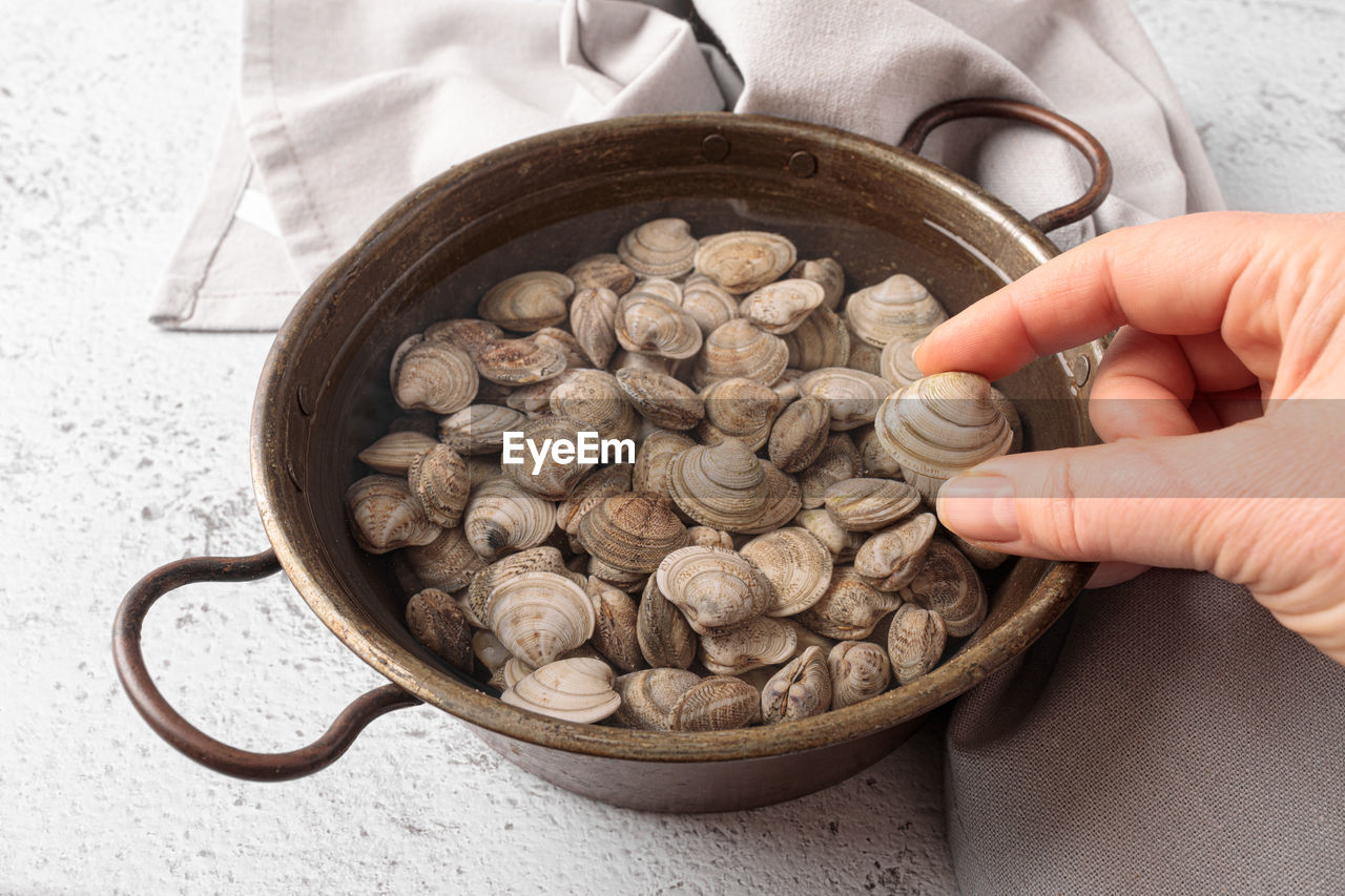 Raw clams in the water inside a copper bowl.