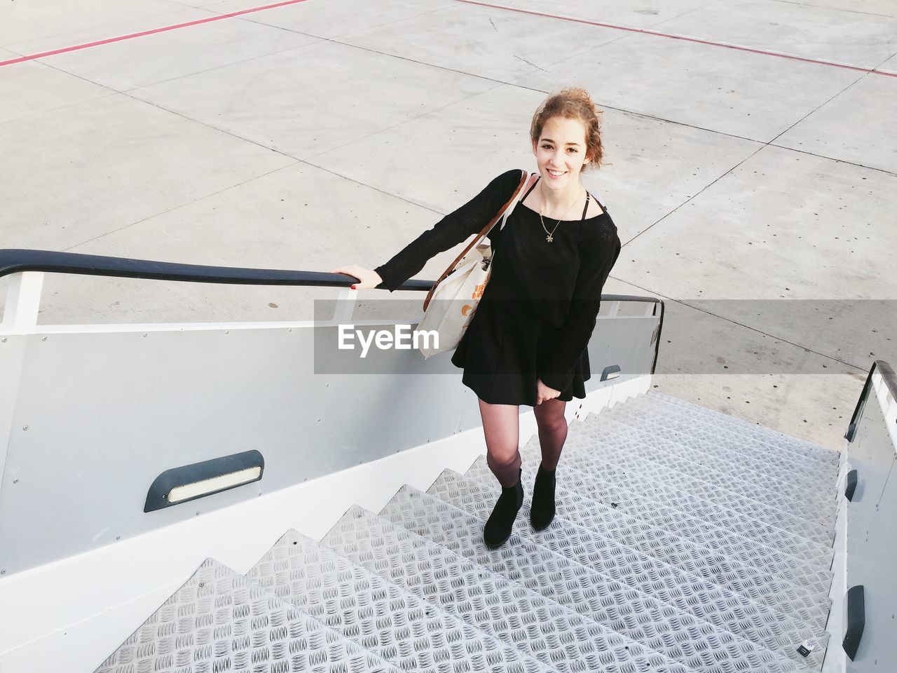 High angle view portrait of woman standing on staircase of airplane at runway