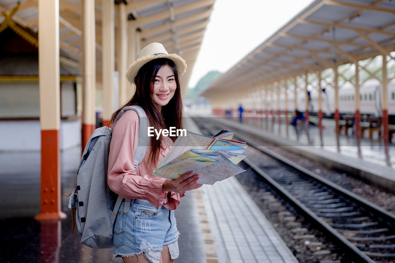 Portrait of woman reading map while standing at railroad station platform