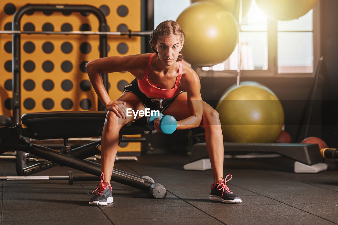 Full length of woman exercising with dumbbell in gym