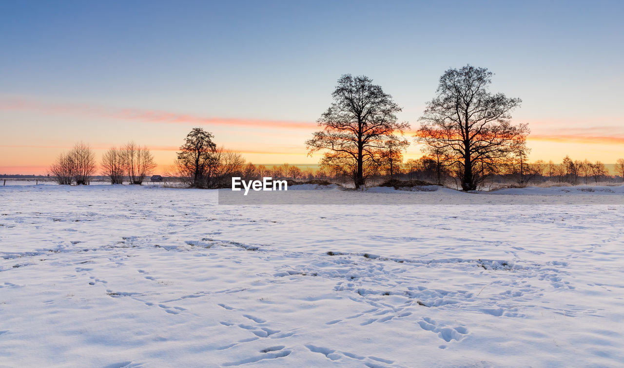 Snow covered field against sky during sunset