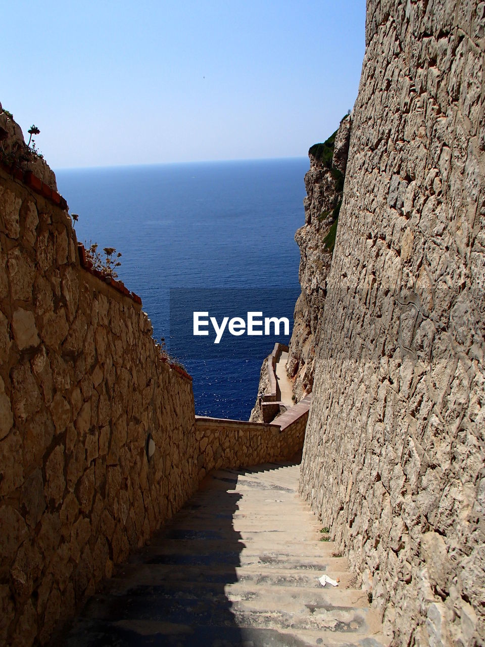 WALKWAY LEADING TO SEA AGAINST CLEAR SKY