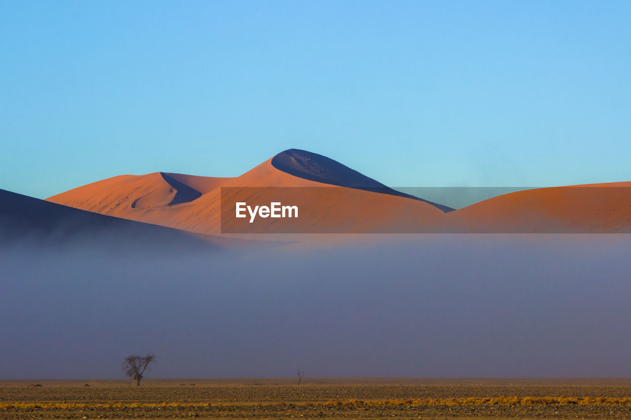 Scenic view of sand dunes against clear blue sky