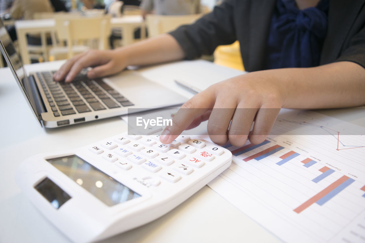 Businesswoman using calculator while working on laptop at table in cafe