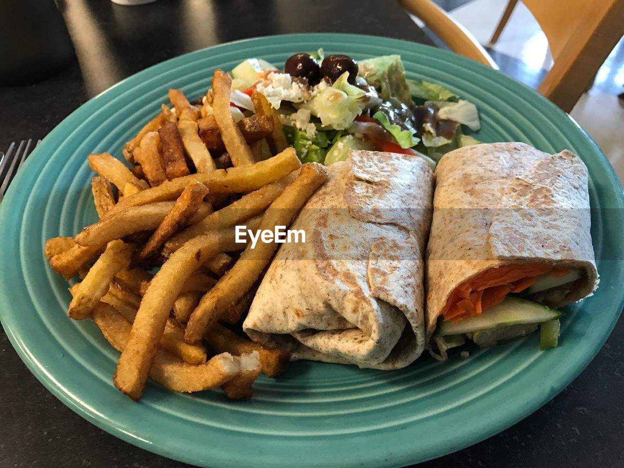 Close-up of spare rib wrap with french fries and greek salad served on table