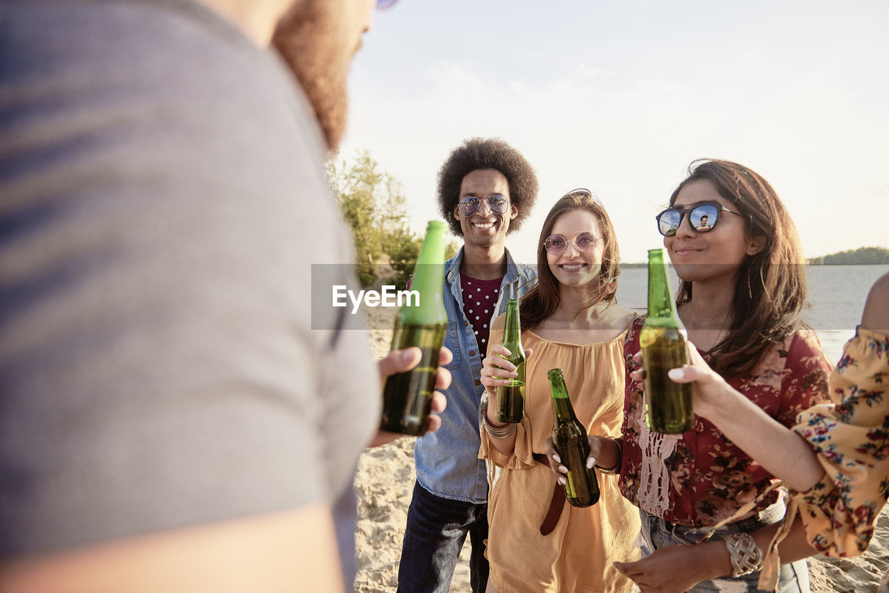 Happy friends with beer bottles standing at beach