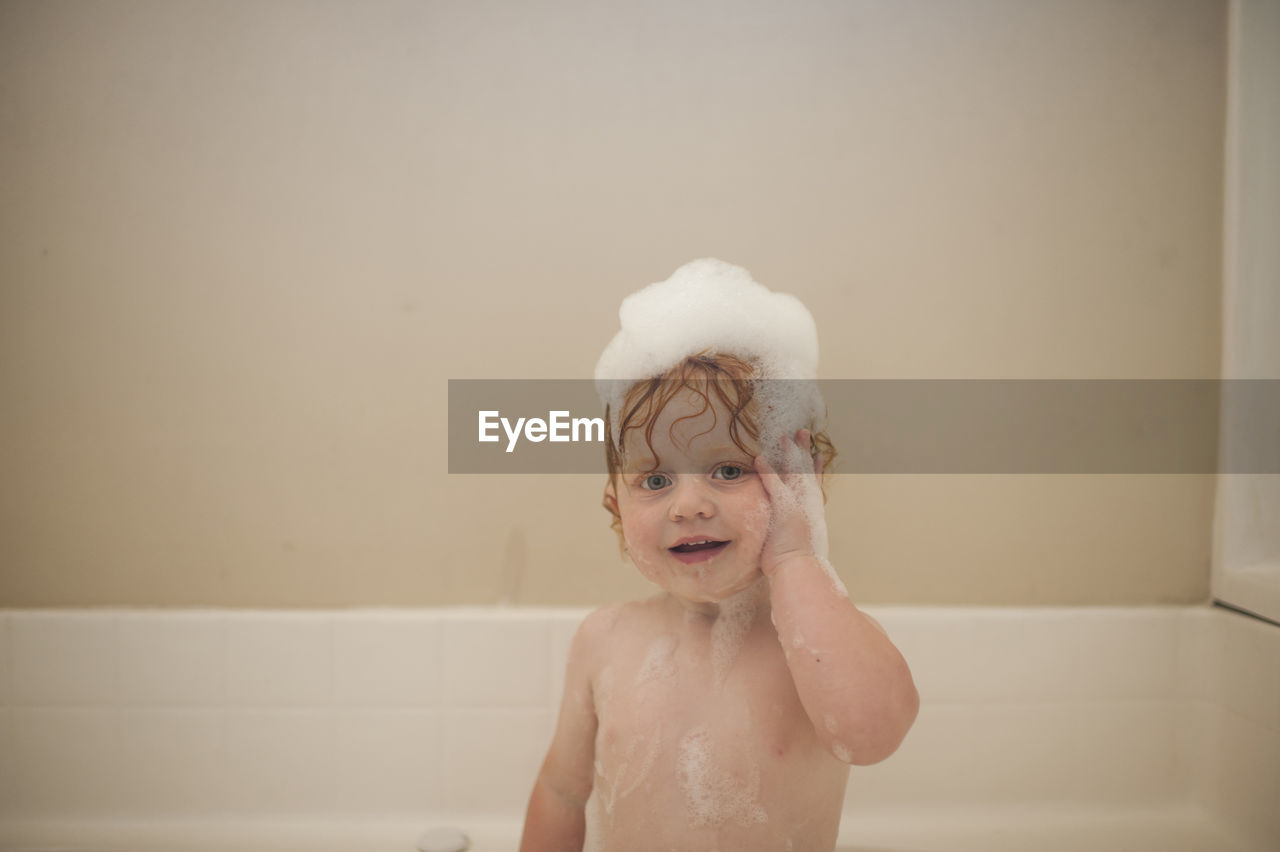 Portrait of cute baby boy bathing in bathtub at home