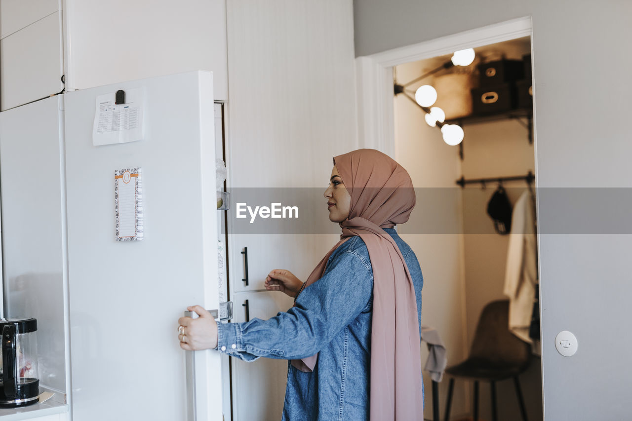 Smiling woman at home opening fridge