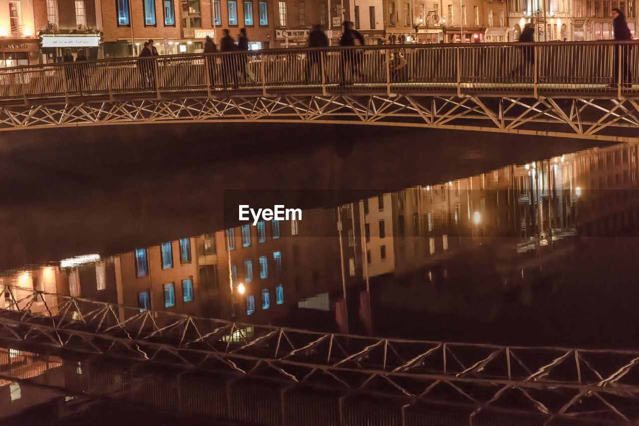 People walking on bridge over river in city at night