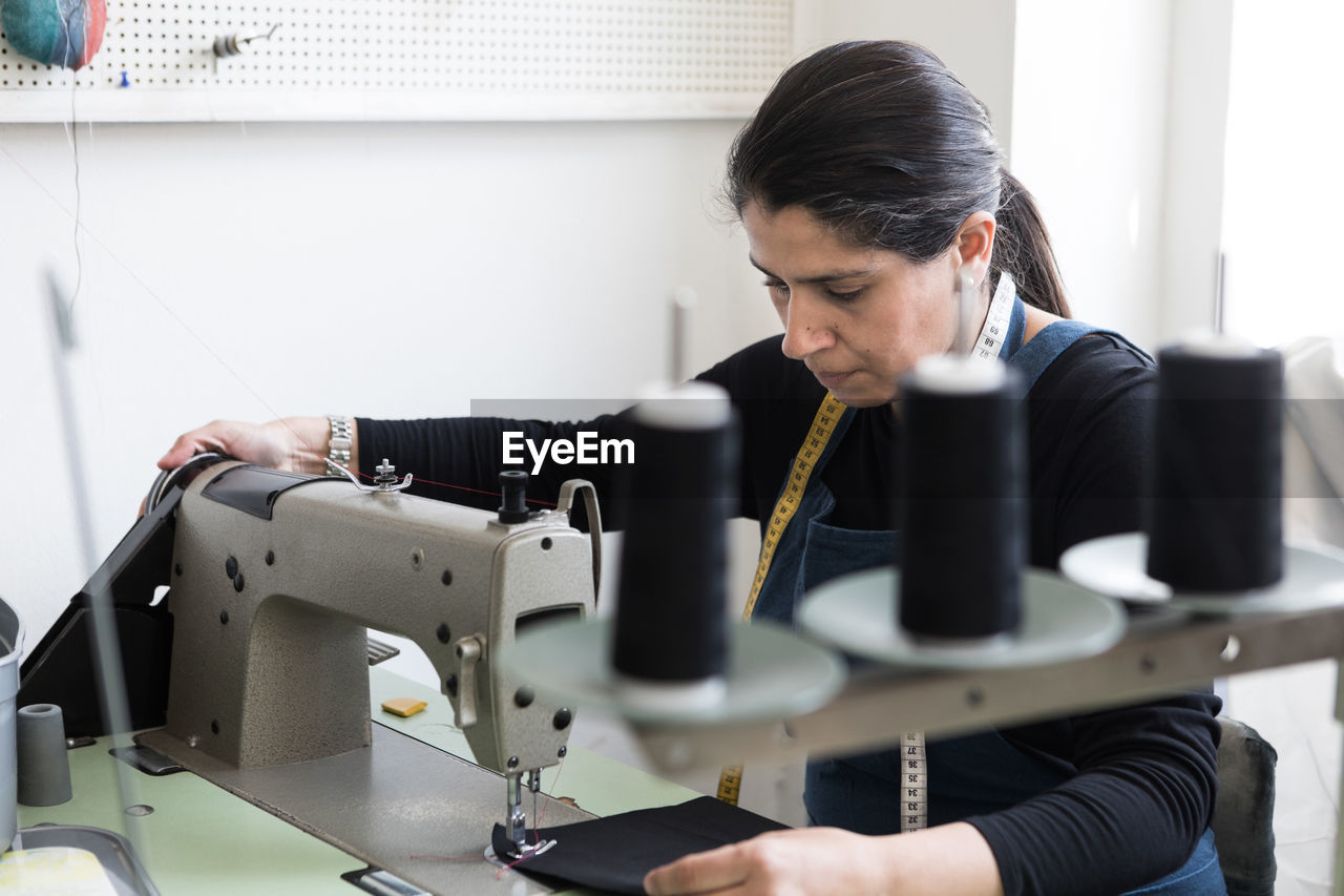 Mature female tailor sewing fabric with machine at laundromat