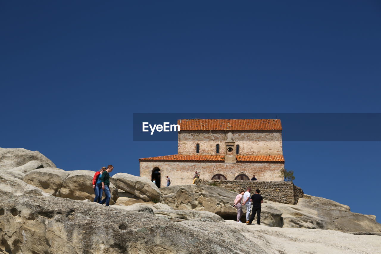 PEOPLE ON ROCKS AGAINST CLEAR BLUE SKY