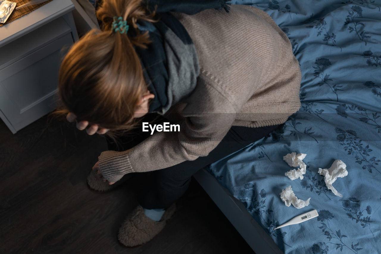 High angle view of sick woman sitting on bed