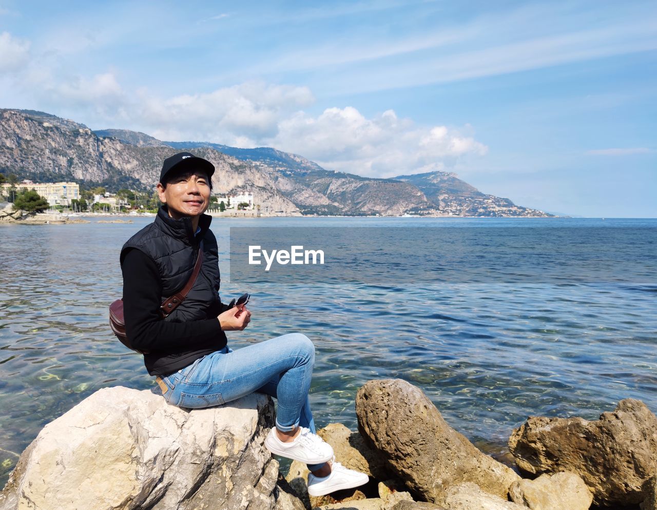 rear view of woman sitting on rock by sea against sky