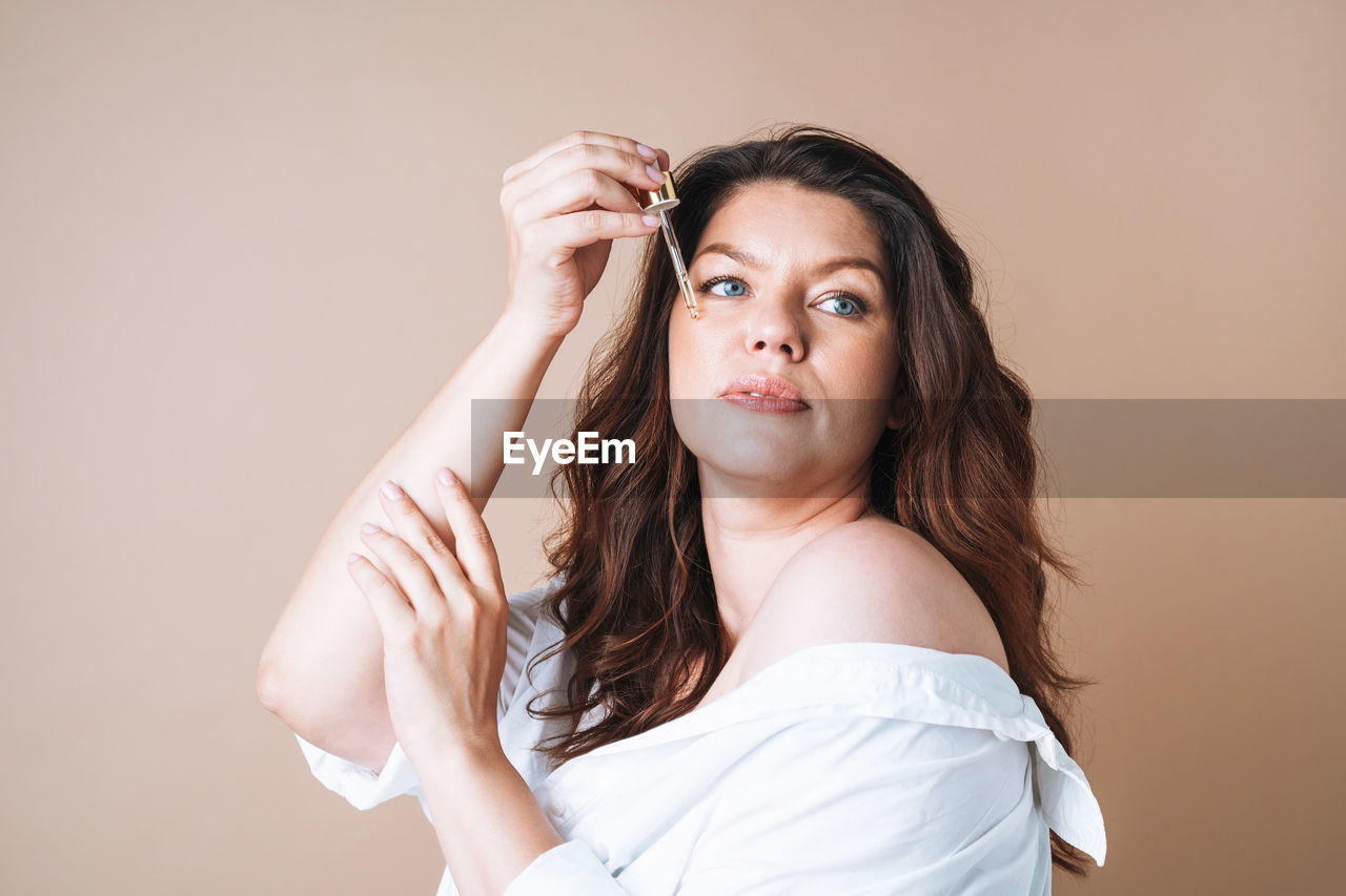 Beauty portrait of woman with pipette with oil on clean fresh skin face on beige background