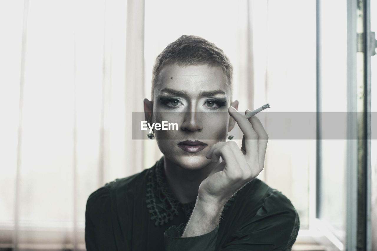 Portrait of genderblend man smoking cigarette at home