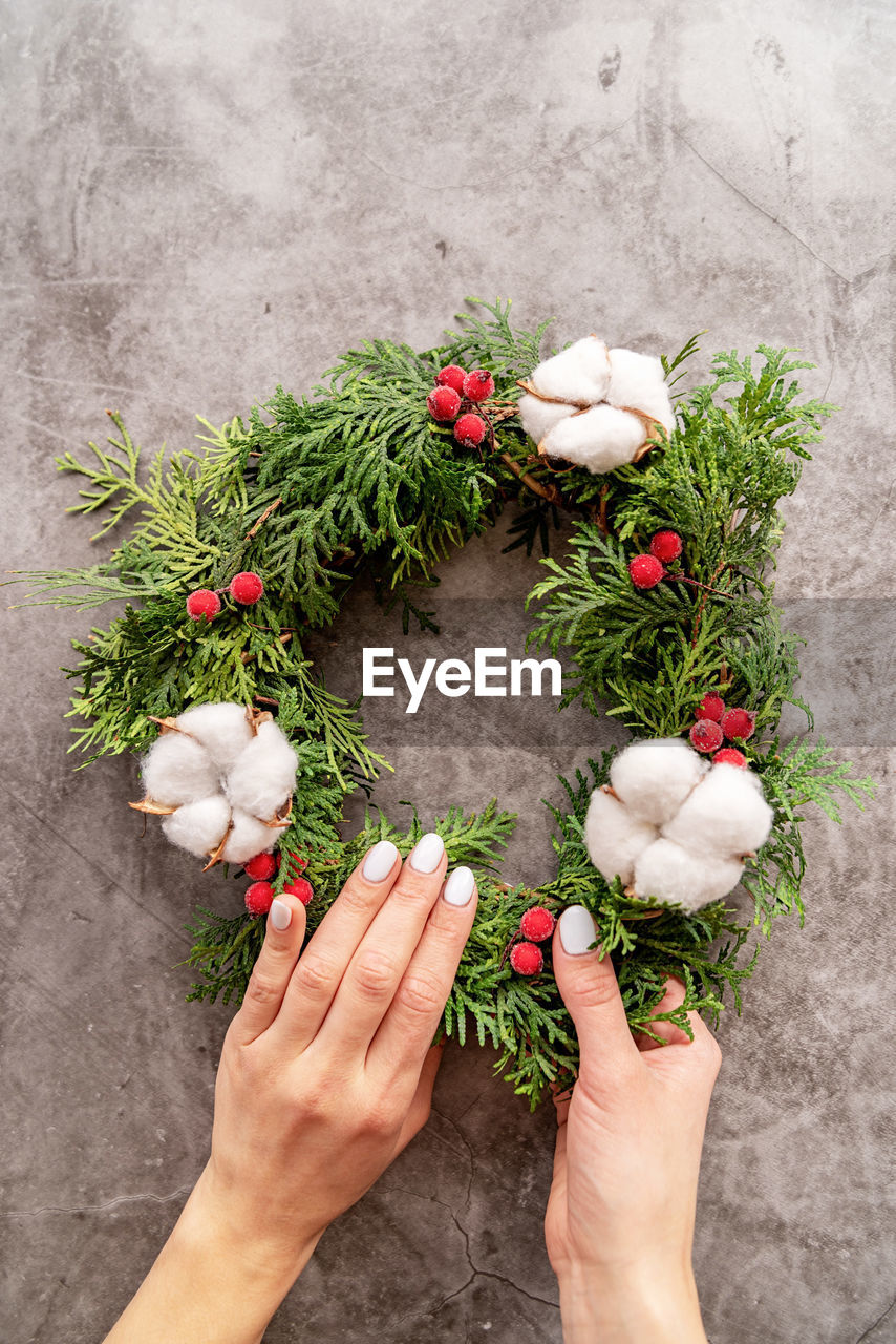 Making christmas wreath with fir tree branches, cotton and red berries top view over dark background