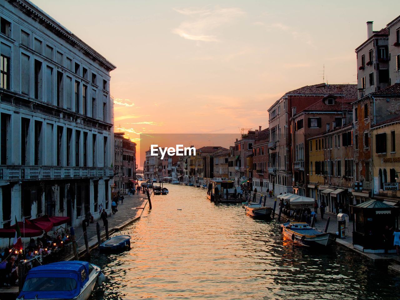 Boats in canal amidst buildings in city during sunset