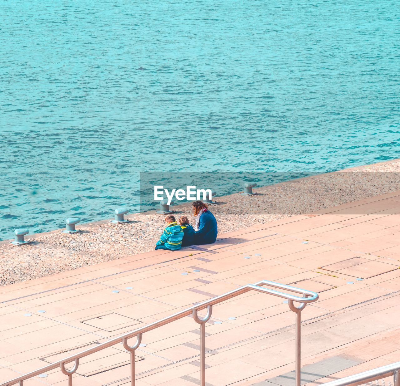 High angle view of family sitting on walkway by sea