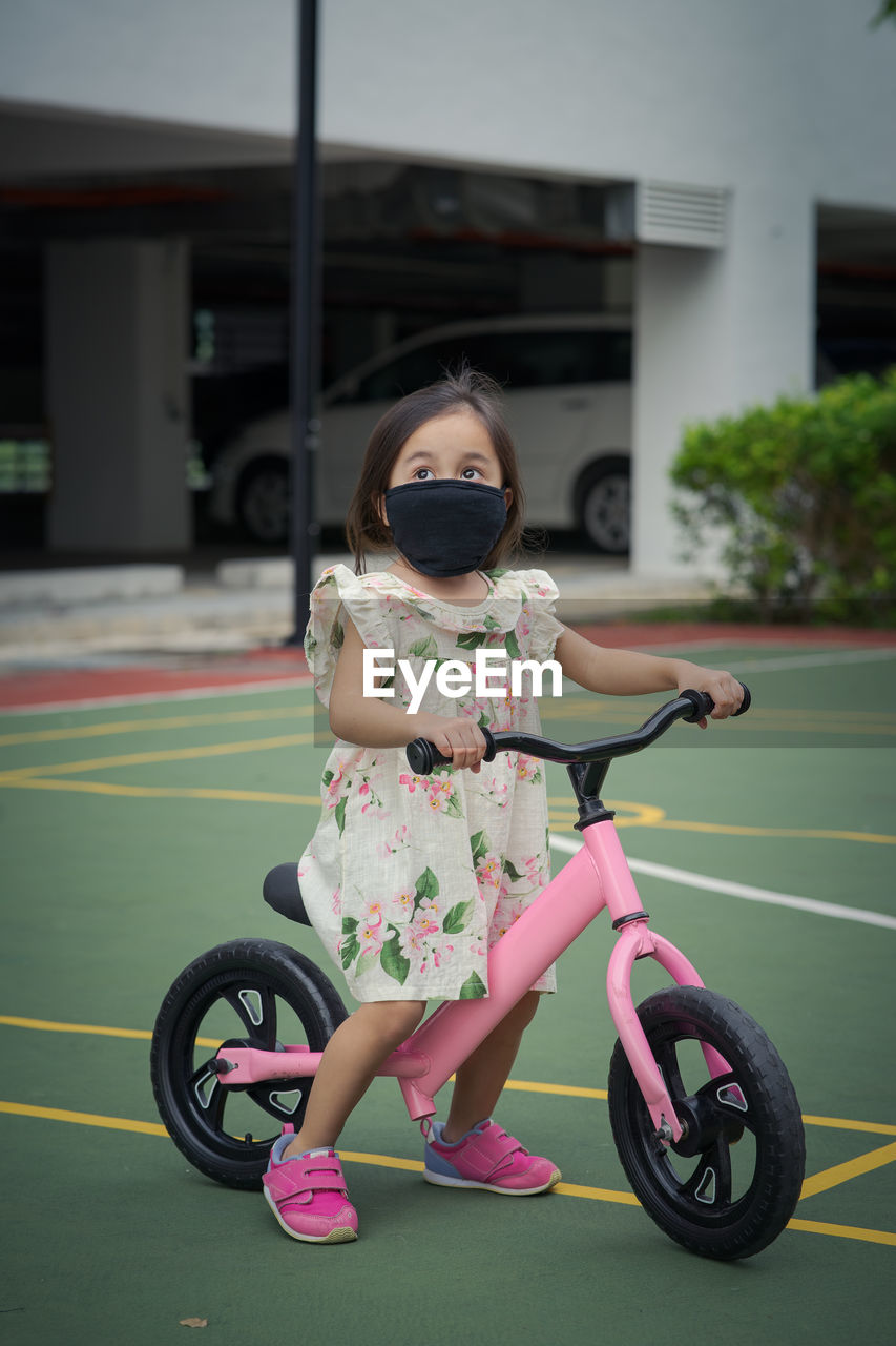 Toddler girl wearing face mask while on a push bike outdoor.