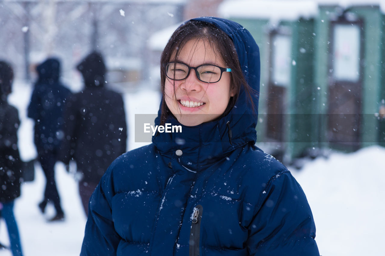 Portrait of smiling girl standing outdoors during snowfall