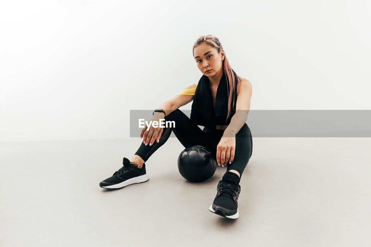 Portrait of young woman sitting on floor against white background