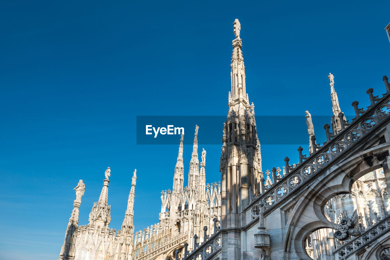 View to spires and statues on roof of duomo through ornate marble fencing. milan, italy