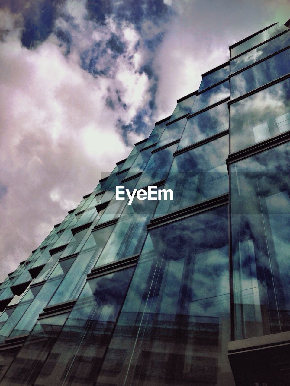 Low angle view of modern glass building against cloudy sky