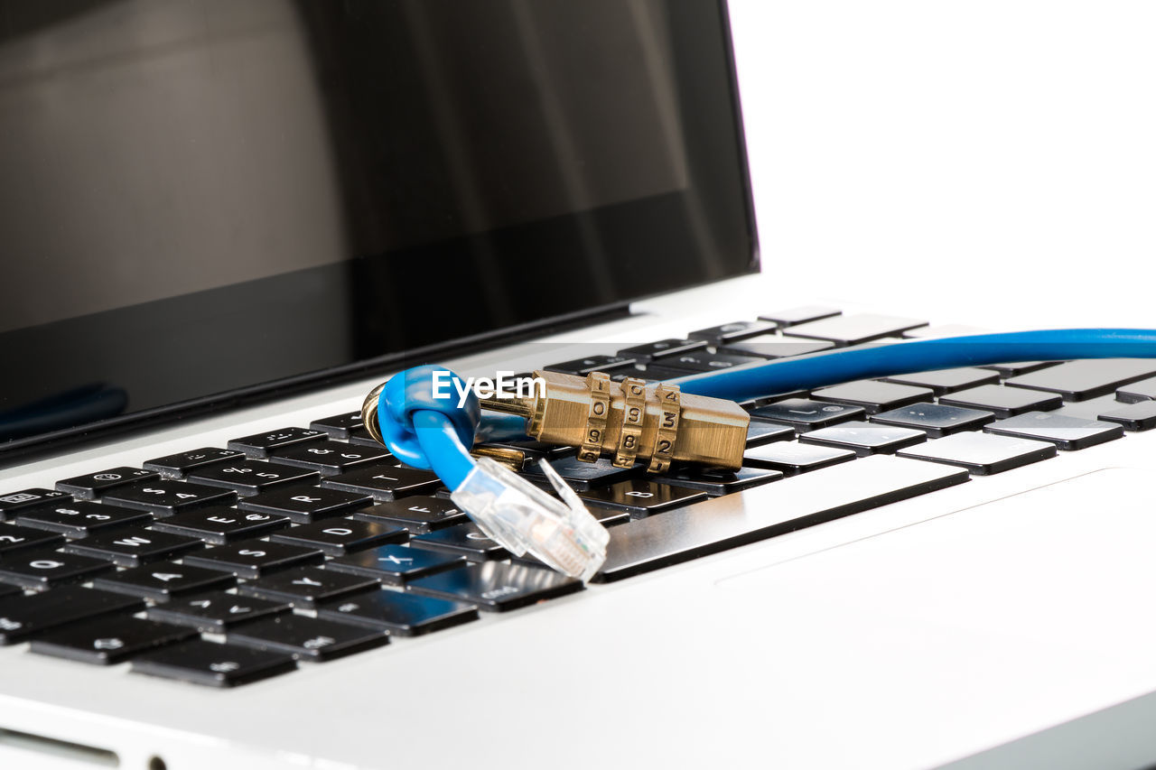 Close-up of padlock and cable on computer keyboard against white background