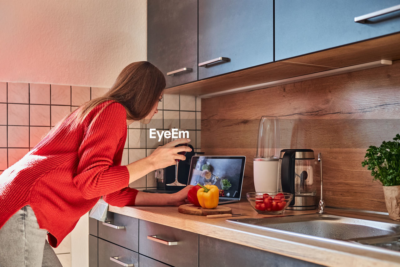 A young woman prepares a salad in the kitchen online and drinks red wine. cooking courses online