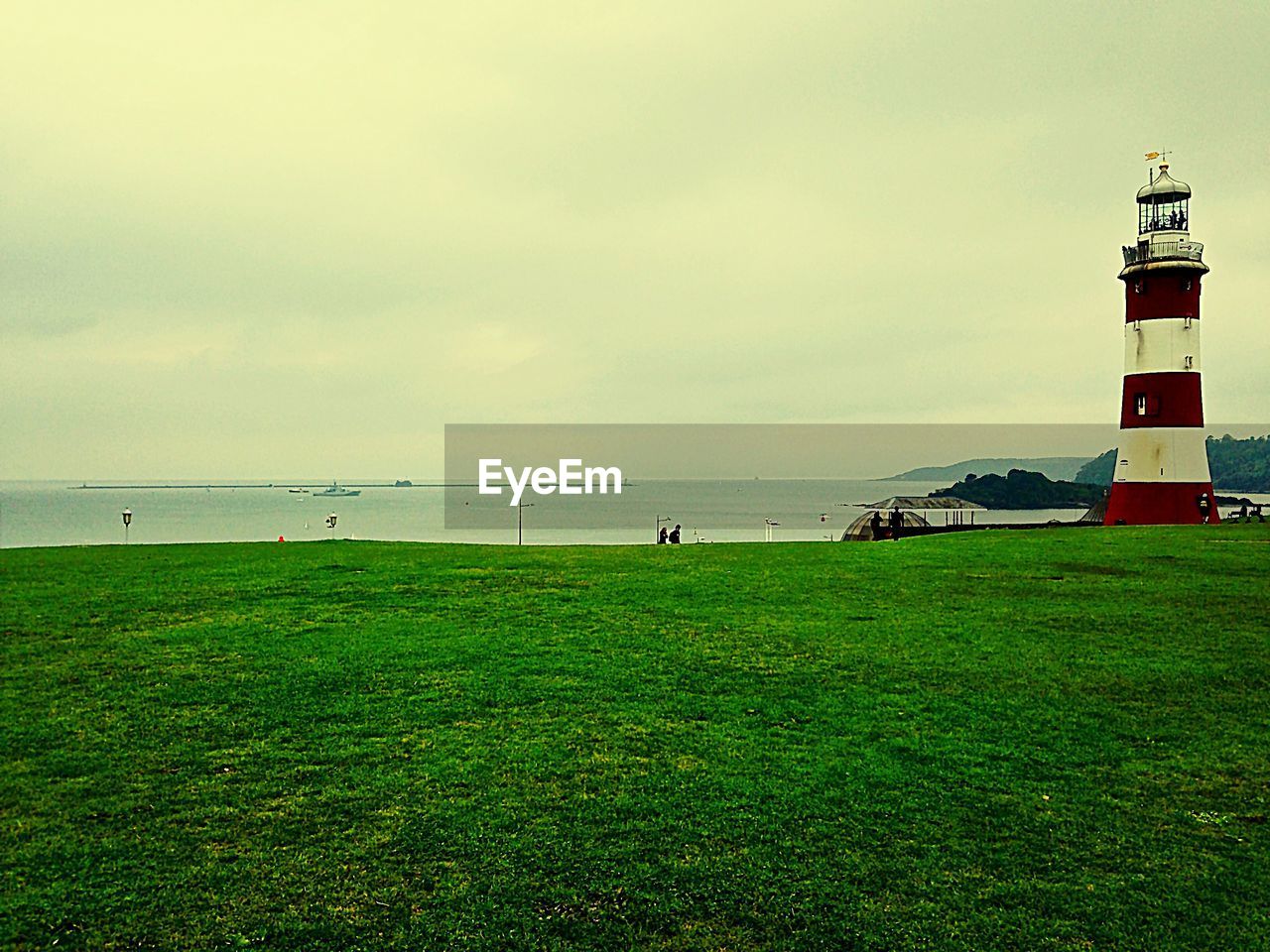 Lighthouse on grassy field in front of sea against sky